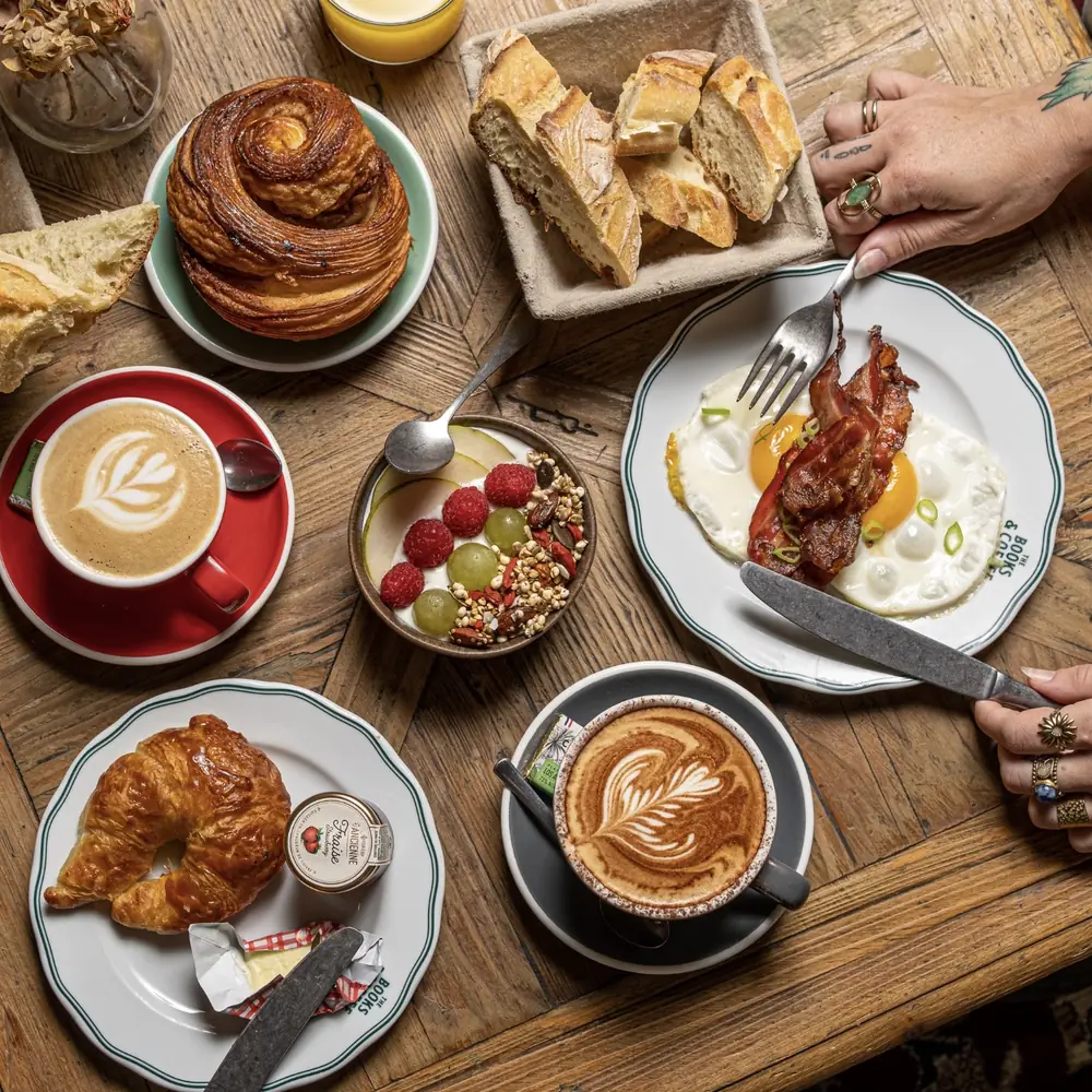 Petit-déjeuner chez Books & Coffee : cafés latte, croissant, brioche, œufs au bacon et bol de granola aux fruits rouges
