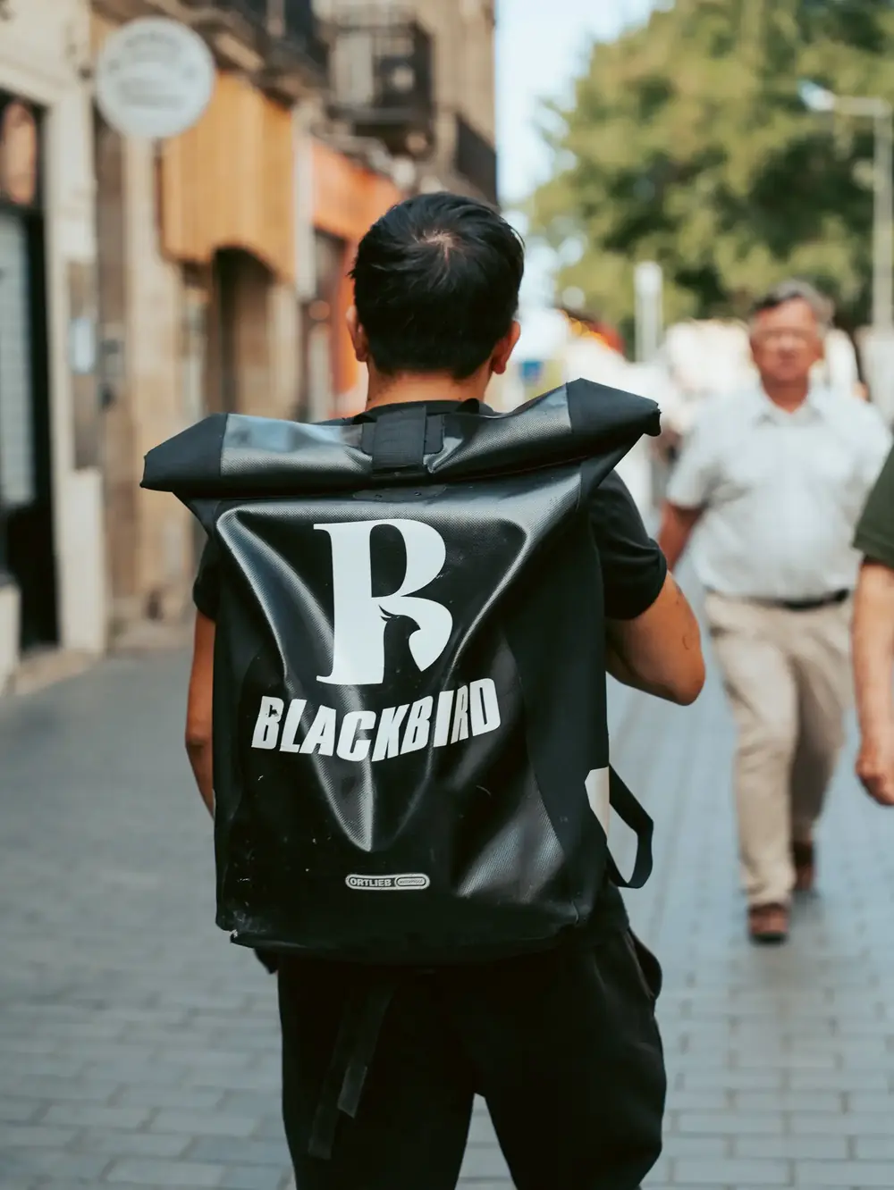 Livreur Blackbird de dos, sac au logo B, dans une rue de Bordeaux