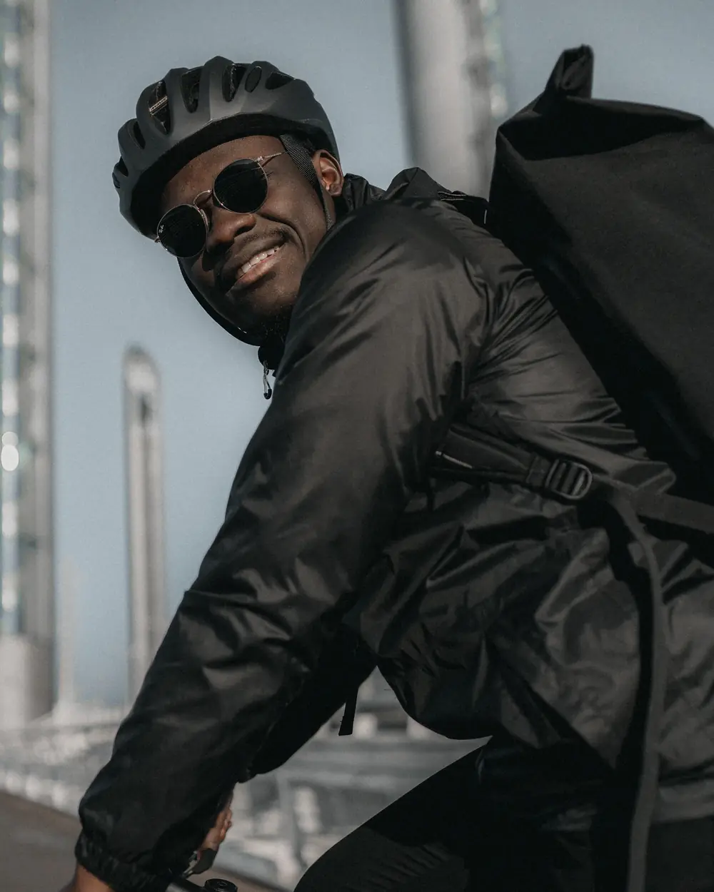 Livreur Blackbird souriant, casque et lunettes de soleil, sac de livraison sur le dos