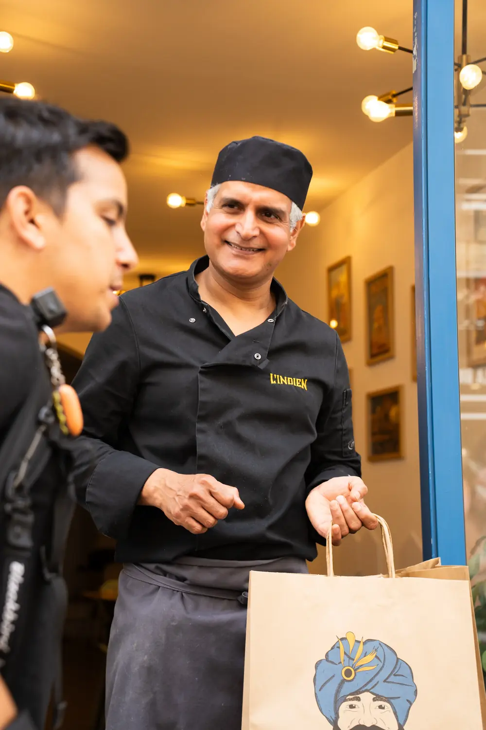 Le chef de L'Indien remet une commande à un livreur Blackbird sur le pas de la porte